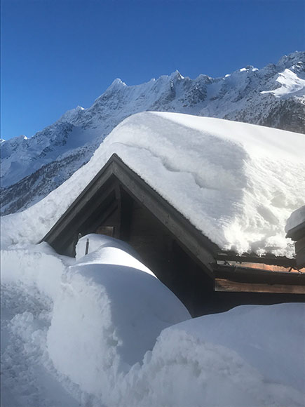 Schneemassen auf Haus mit Berge und blauem Himmel im Hintergrund